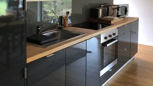A modern kitchen with black cabinets, a wooden countertop, a built-in oven, and a large window.