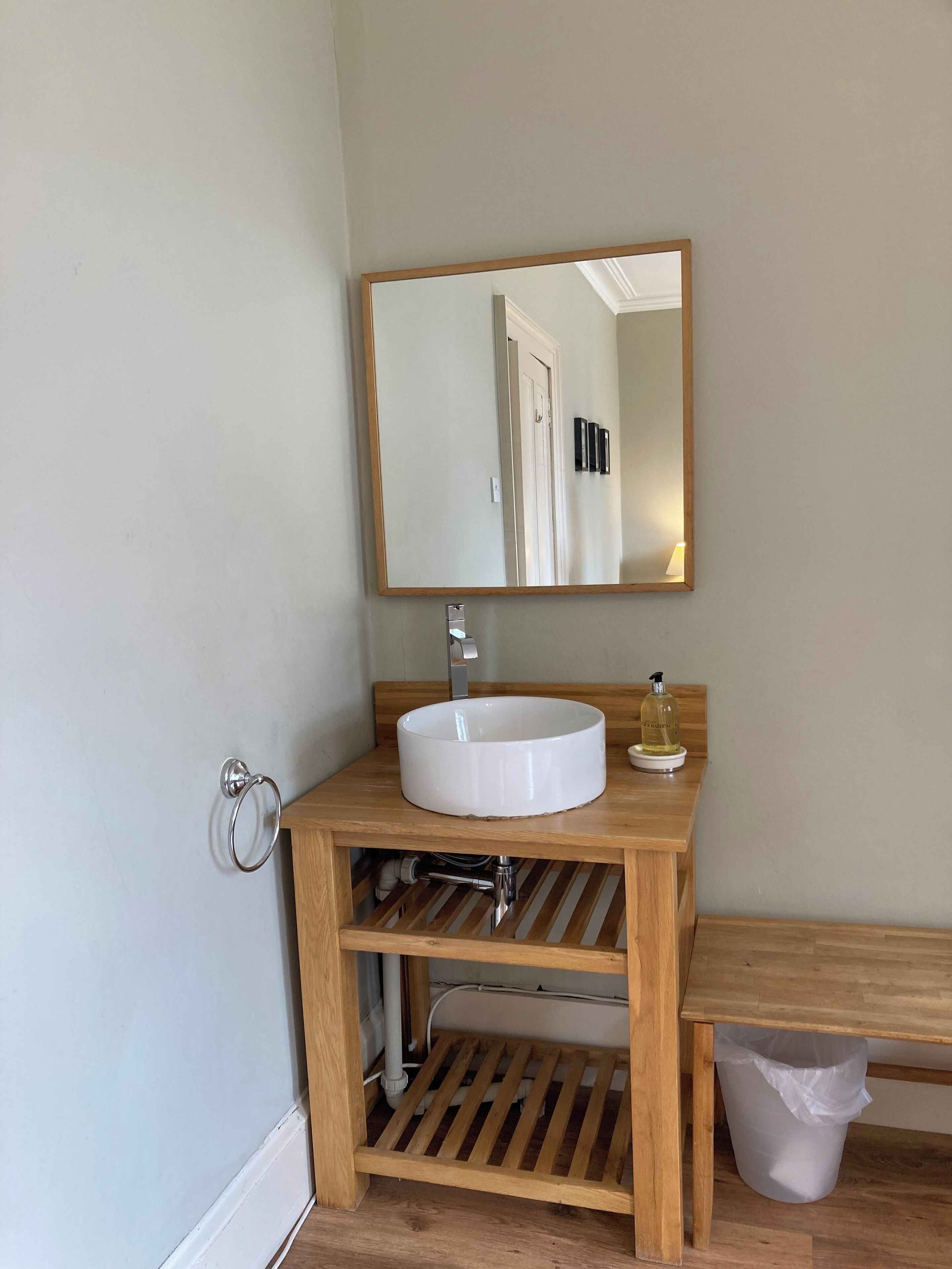 A bathroom with a wooden vanity, a white sink, a mirror, and a trash bin.