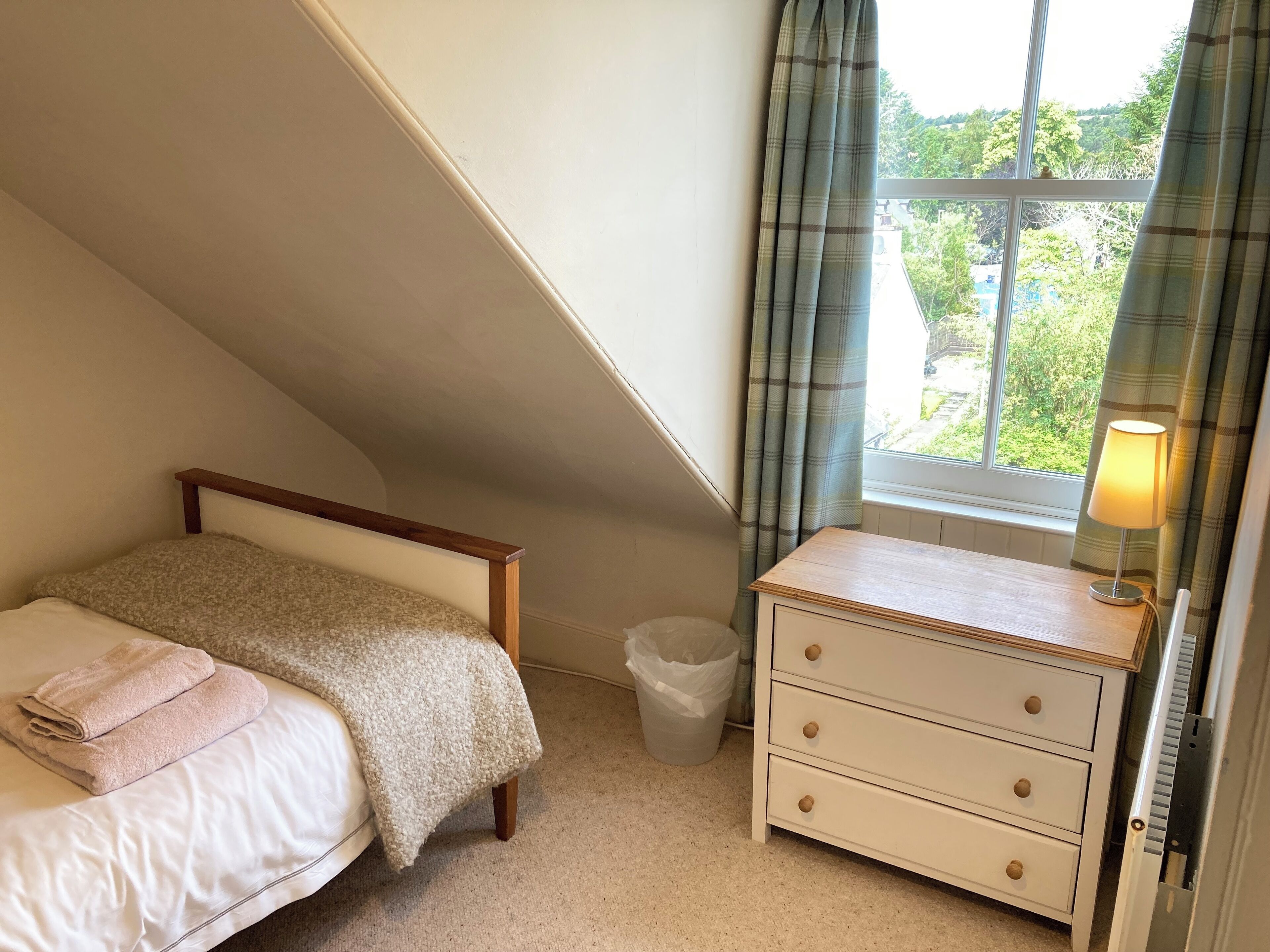 Un dormitorio con cama, mesita de noche, lámpara y ventana con cortinas.