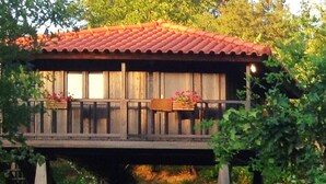 A wooden house with a red-tiled roof, a balcony with flower boxes, and a dining table set up outside. - Pool Villa Espigueiro I (Arcos de Valdevez)