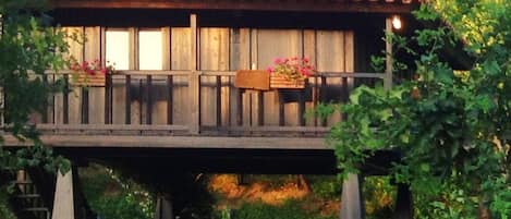 Una casa de madera con techo de tejas rojas, un balcón con macetas de flores y una mesa de comedor instalada afuera.
