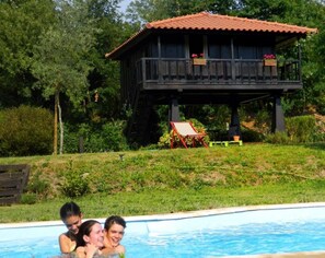 A wooden cabin with a red roof, a pool, and a grassy area with a chair and table.