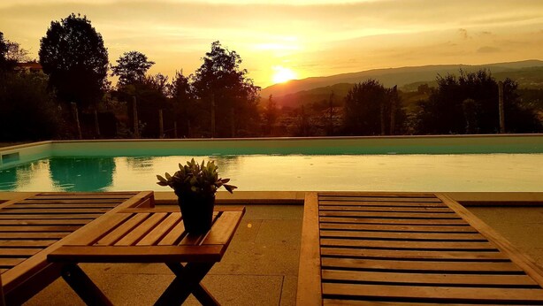 A poolside area with wooden loungers and a potted plant, overlooking a swimming pool and a sunset view. - Pool Villa Espigueiro I (Arcos de Valdevez)