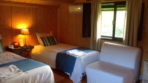 Une chambre de style cabane avec deux lits simples, un canapé, une table de chevet avec une lampe et une fenêtre avec des rideaux.