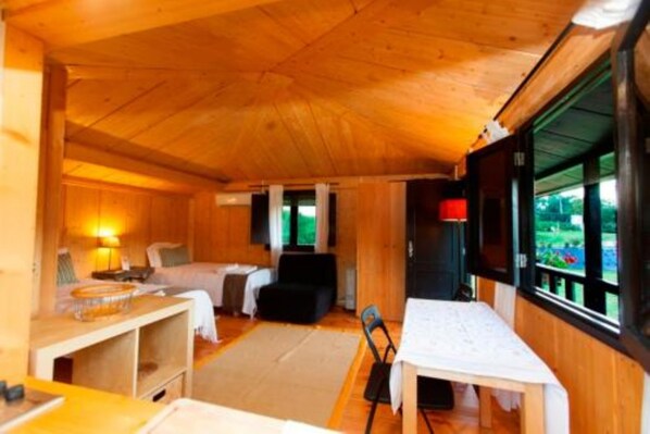 Interior acogedor de una cabaña con techo de madera, una cama, una mesa de comedor y una ventana con vista a la vegetación.