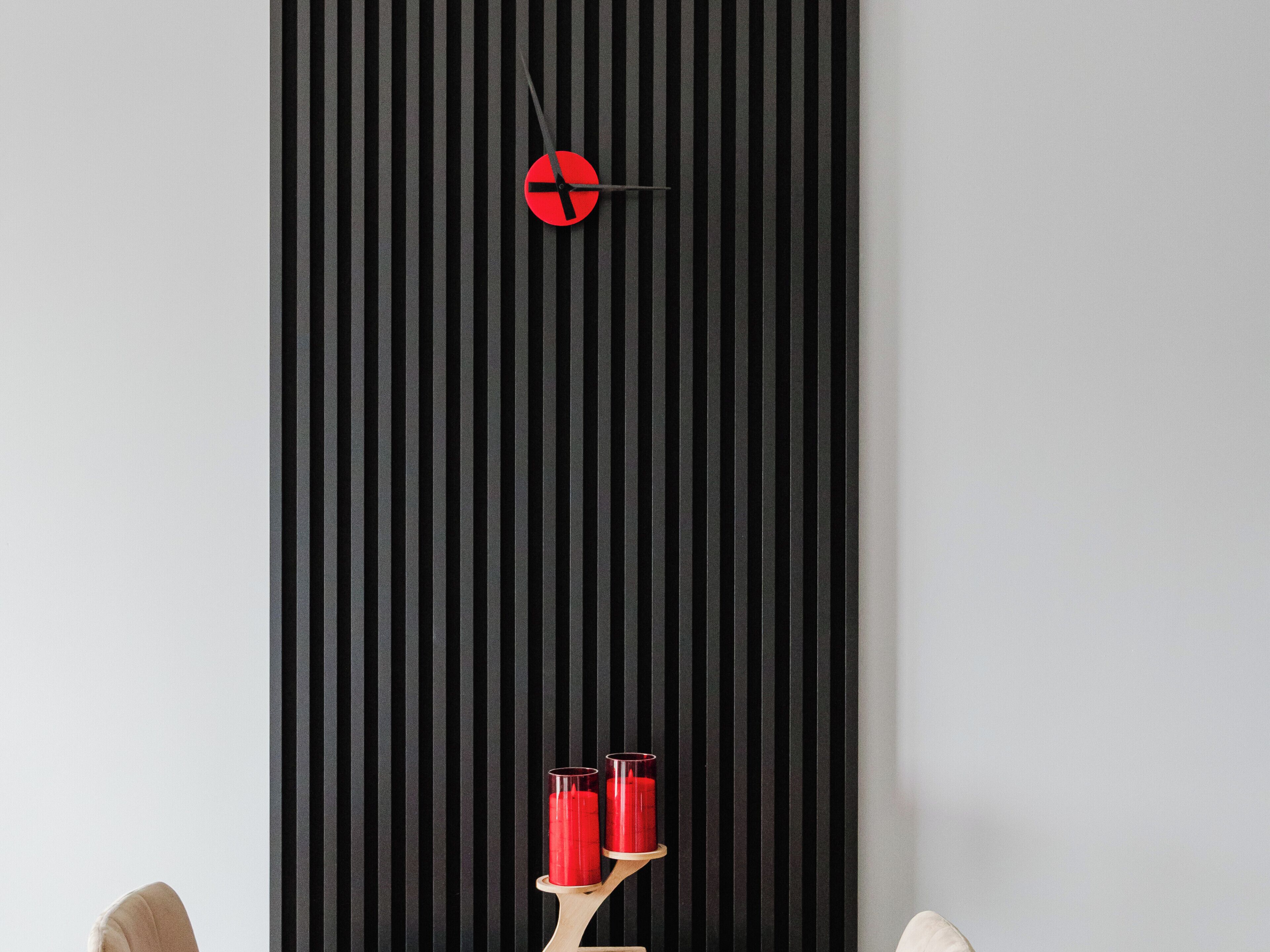 Una habitació moderna amb una paret de bandes negres, un rellotge minimalista i dues espelmes vermelles sobre un suport de fusta.