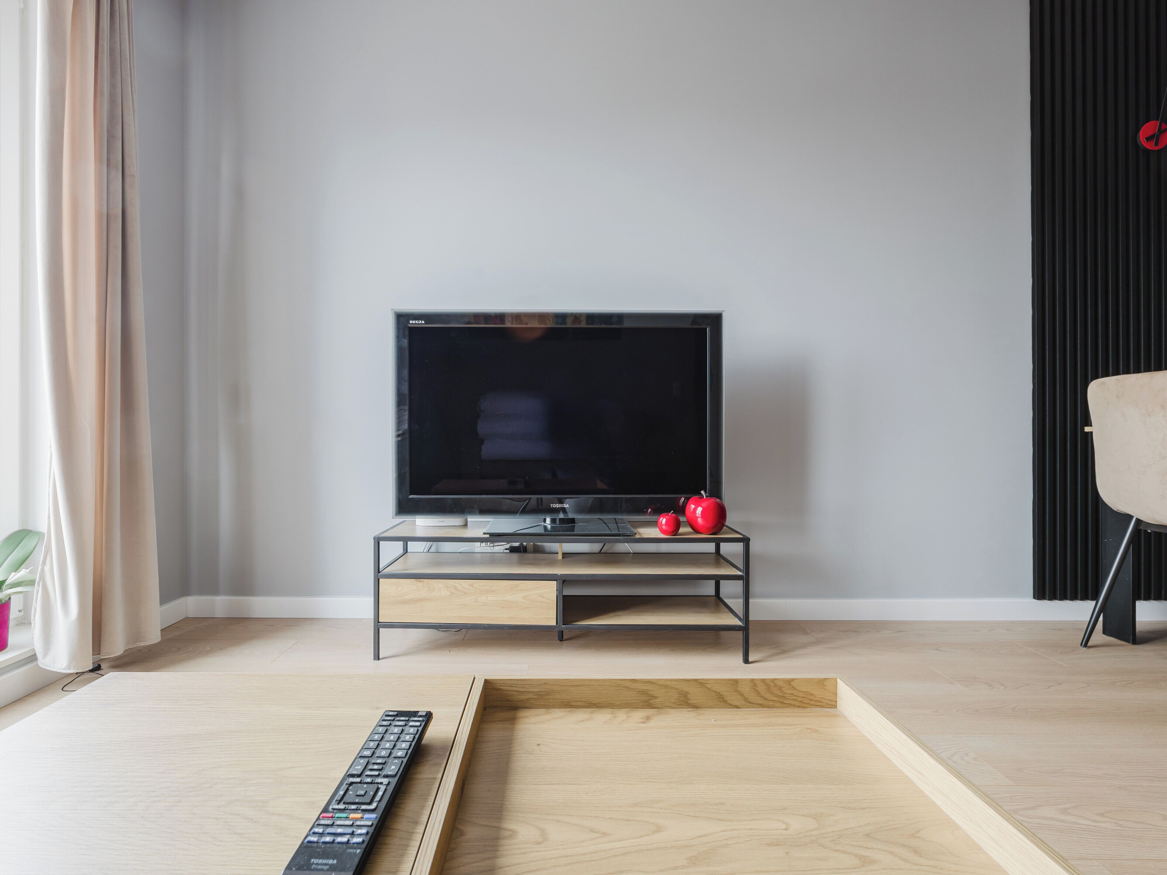 Un salon moderne avec un téléviseur à écran plat posé sur un meuble télé en verre, une table basse en bois et une pomme rouge sur le meuble.