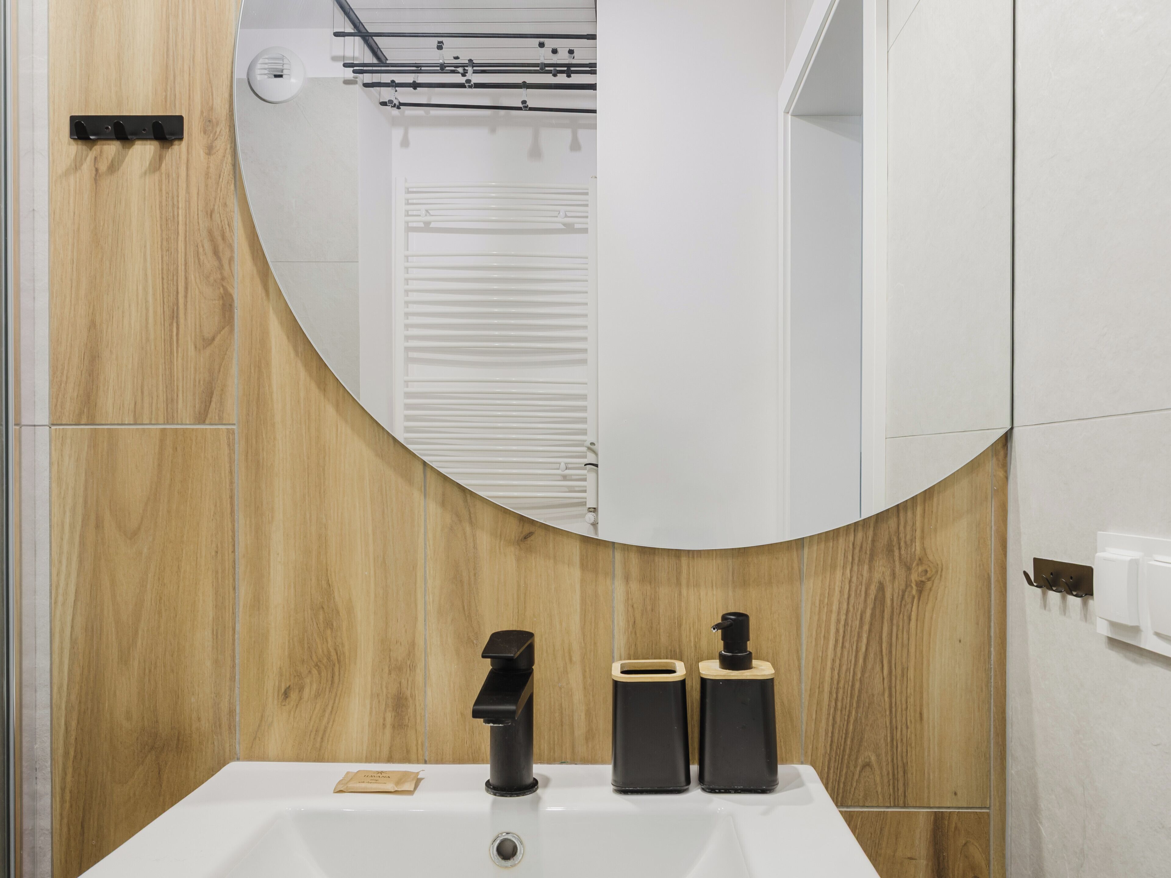 A bathroom with a wooden wall, a white sink with a black faucet, and two black soap dispensers.