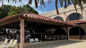 A pool area with a covered seating area, lounge chairs, and a building with arched windows in the background. - Coronado Luxury Club & Suites - swim up with golf for 2 and resort amenities! (Panamá Oeste Province)
