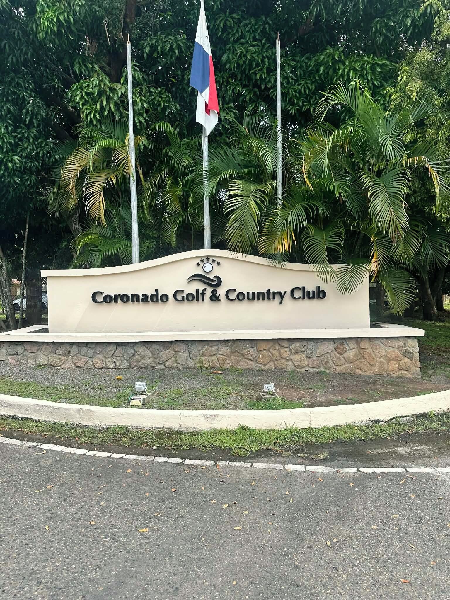 Une enseigne indiquant l’emplacement du Coronado Golf & Country Club, avec un drapeau et des palmiers en arrière-plan.