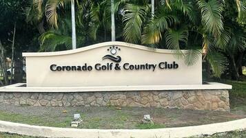 Une enseigne indiquant l’emplacement du Coronado Golf & Country Club, avec un drapeau et des palmiers en arrière-plan.