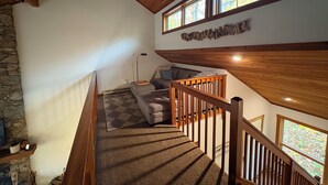 Eine Holztreppe mit Schachbrettmuster-Teppich, der zu einem Wohnbereich mit Sofa und Steinwand führt.