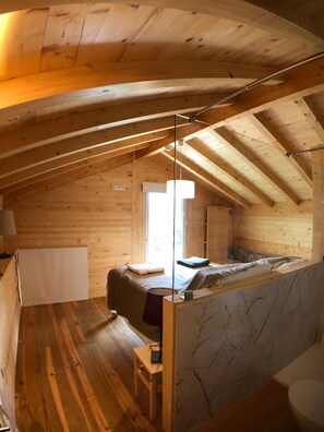 Una cabaña de madera con habitación en el altillo, un baño con encimera de mármol y un amplio ventanal que proporciona luz natural.