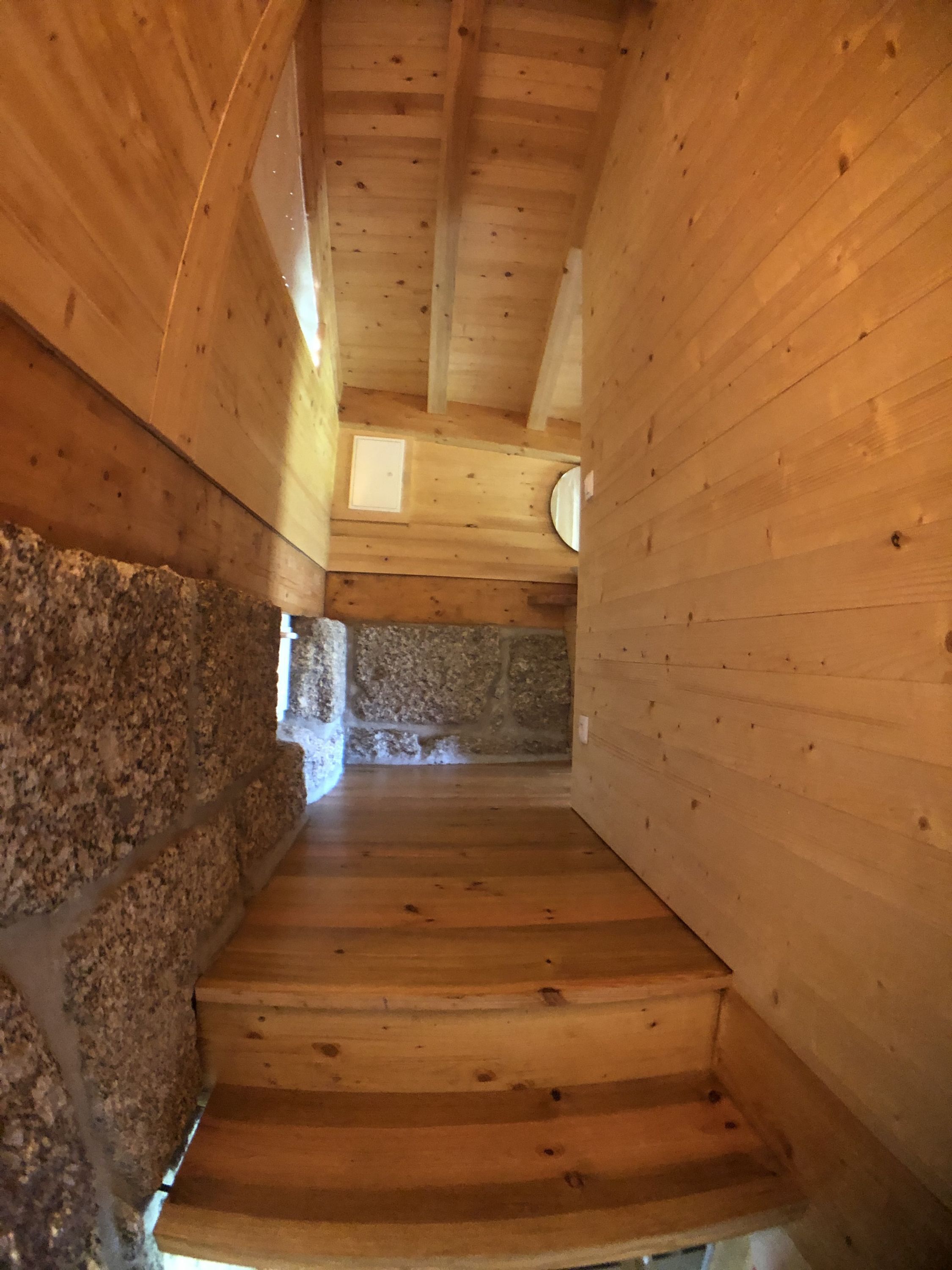 Una escalera de madera con un muro de piedra a un lado y un muro de madera al otro, que conduce a un nivel superior.