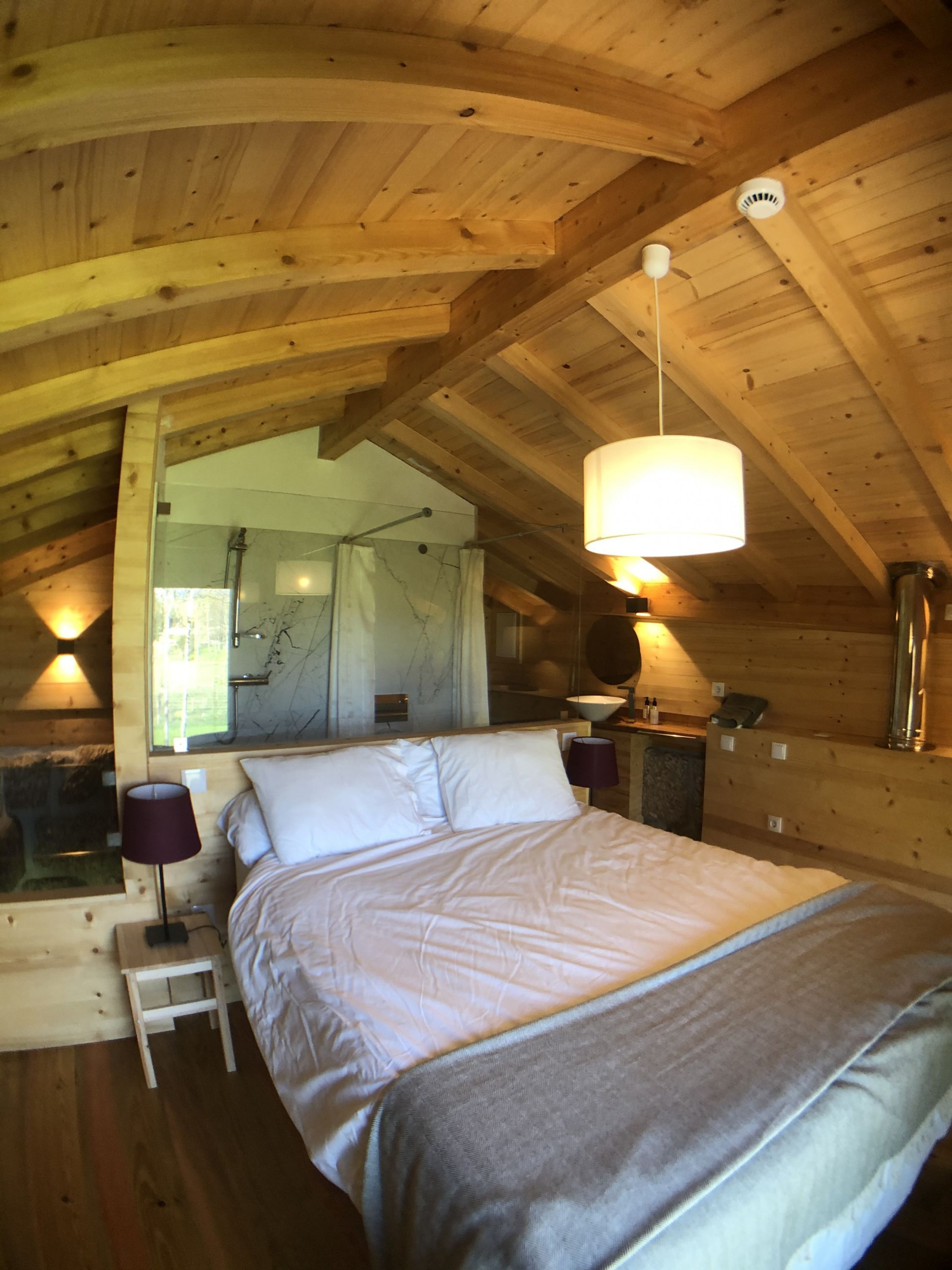 A cozy wooden cabin bedroom with a bed, bedside lamps, and a hanging light fixture.