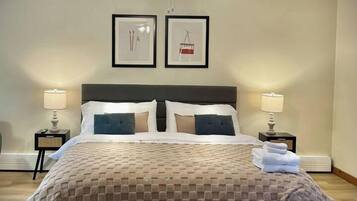 A neatly made bed with a checkered bedspread, two bedside lamps, a ceiling fan, and two framed pictures on the wall.