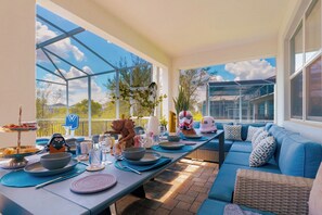 Un espacio exterior para comer con una larga mesa dispuesta para una comida, rodeado por un sofá azul y un banco de mimbre.