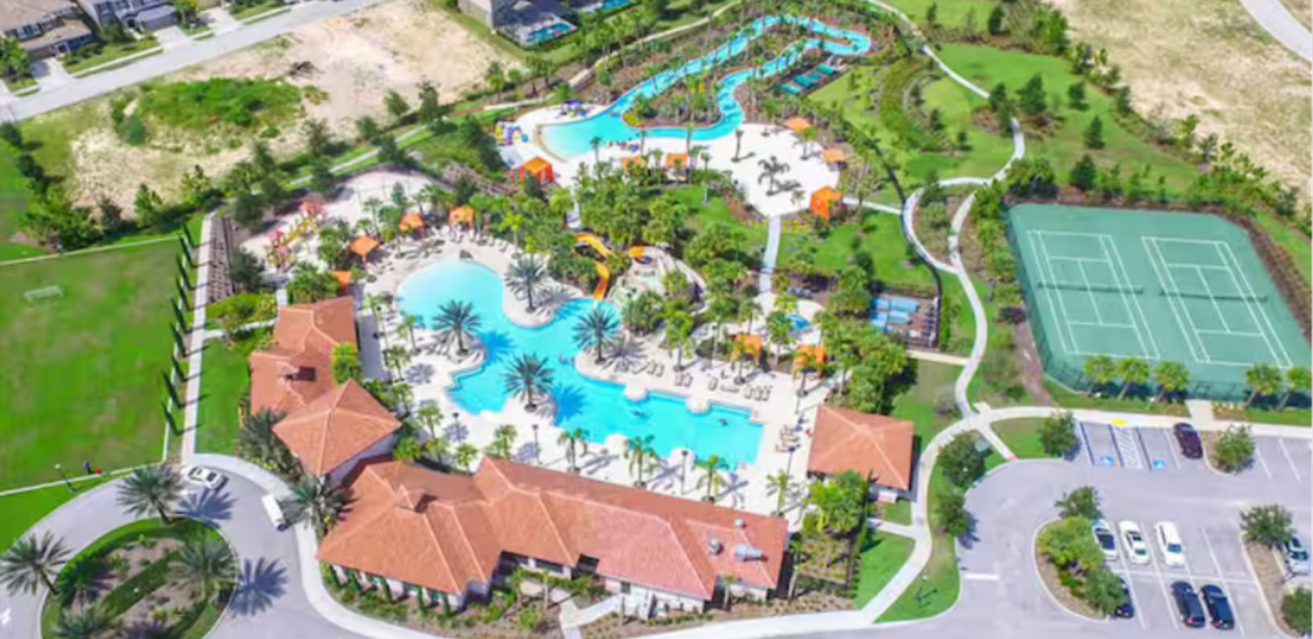Una vista aerea di un resort con una piscina centrale, diverse scivoli d'acqua e campi da tennis.