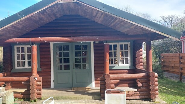 A rustic log cabin with a green door, two windows, and a porch. - Small rustic log cabin, centrally located on the Isle of Skye. (Broadford)