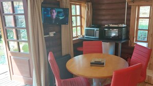 A cozy corner with a wooden table and red chairs, a TV mounted on the wall, and a microwave on a shelf. - Small rustic log cabin, centrally located on the Isle of Skye. (Broadford)
