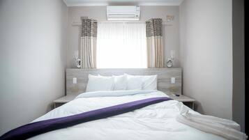 A hotel room with a bed, a nightstand, a window with curtains, and an air conditioning unit.