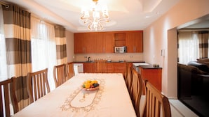 Un comedor con una mesa dispuesta para cuatro personas, un frutero, sillas de madera, una araña y armarios de madera.