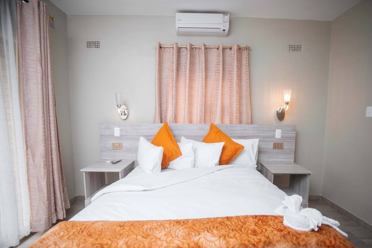 A hotel room with a bed, two nightstands, an air conditioning unit, and a shower curtain.