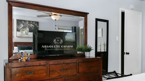 A bedroom with a wooden dresser, a flat-screen TV, a ceiling fan, and a framed floral artwork. - Karen's Kottage | 3/2, Hot Tub, Fireplace, Fire-pit & Grill, Man Cave w/ Games + Bar (Fredericksburg)