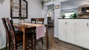 A dining area with a wooden table and chairs, white cabinets, and a decorative metal gate. - Karen's Kottage | 3/2, Hot Tub, Fireplace, Fire-pit & Grill, Man Cave w/ Games + Bar (Fredericksburg)
