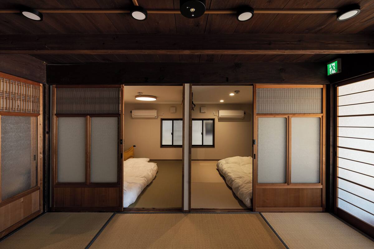 A traditional Japanese room with tatami flooring, sliding doors, and a bed with white bedding.