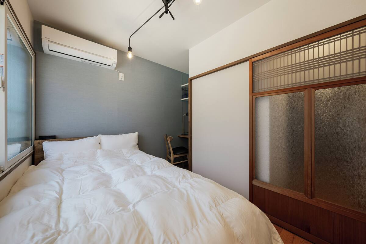 A bedroom with a large bed, a window, an air conditioning unit, and a wooden wardrobe.