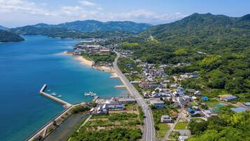 An aerial view of a coastal town with a long road, a beach, and a mountainous backdrop.