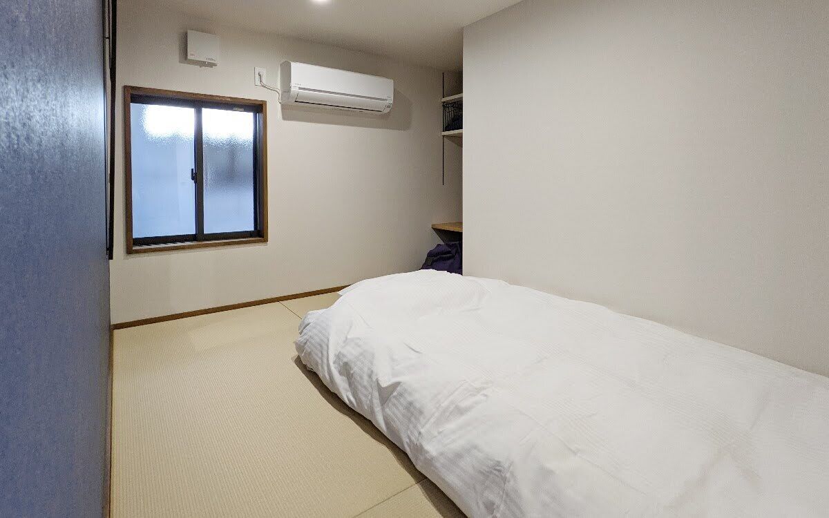 Una habitación pequeña y limpia con una cama individual, ventana y aire acondicionado.