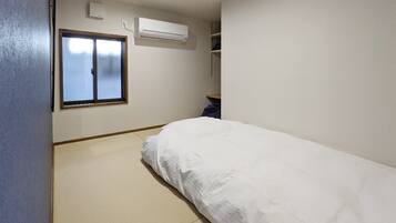 Una habitación pequeña y limpia con una cama individual, ventana y aire acondicionado.