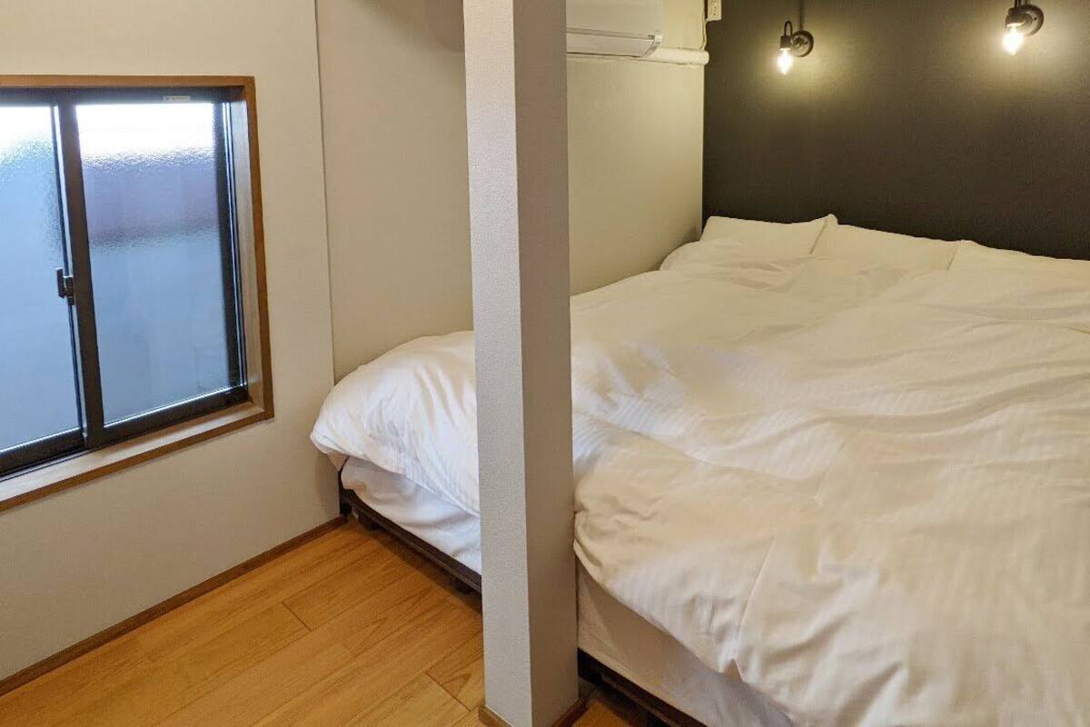 A bedroom with a bed, a window, and a wall-mounted light fixture.