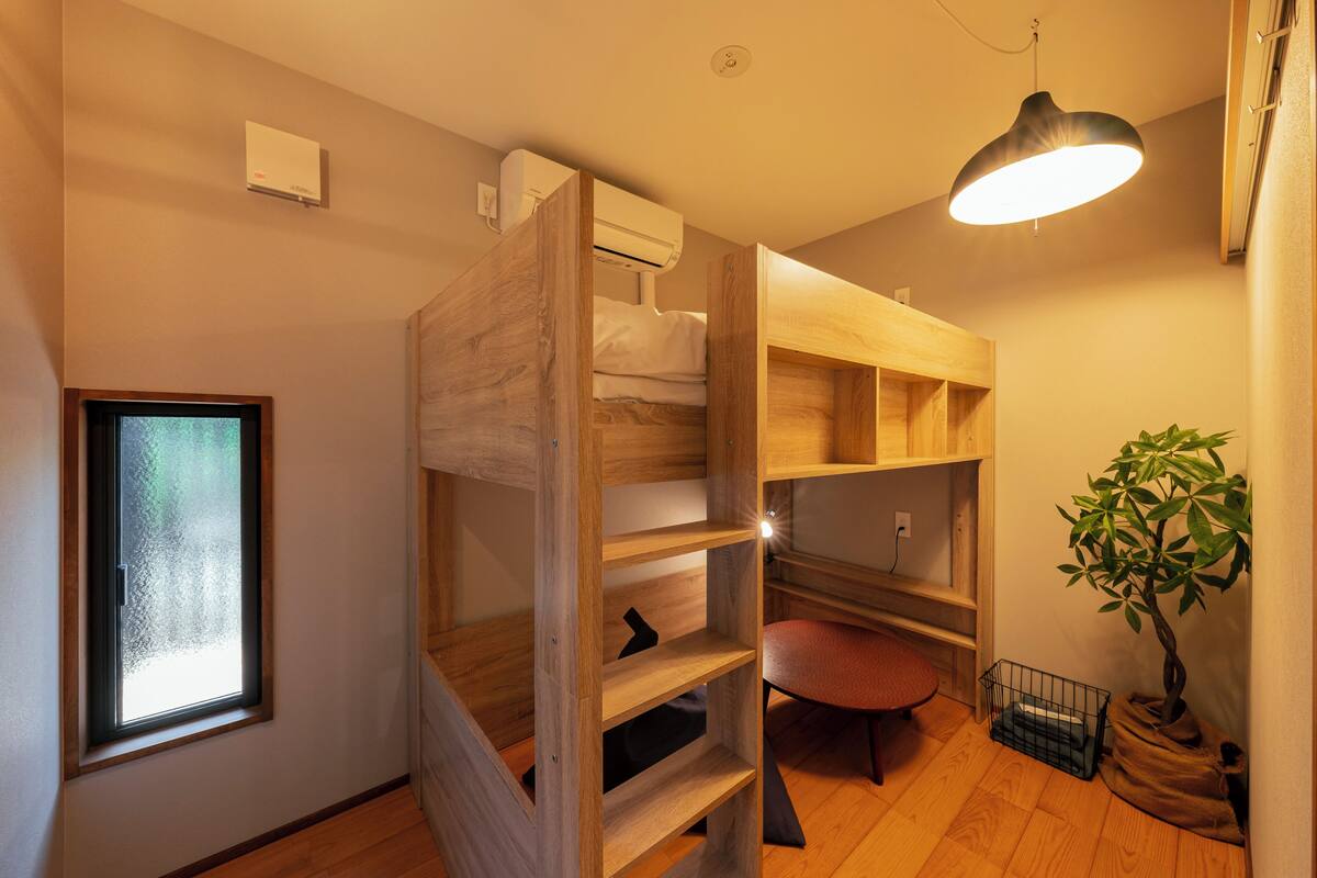 A compact room with a bunk bed, a desk, a chair, a potted plant, and a window.