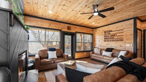 A modern log cabin interior with leather sofas, a fireplace, and a wall sign welcoming visitors to the Great Smoky Mountains. - NEW, INDOOR POOL, GAME ROOM, BUNK ROOM, HOT TUB (Sevierville)