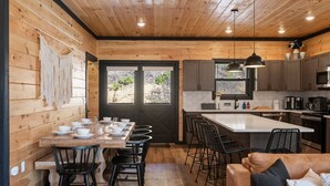 A wooden interior with a dining table set for four, a kitchen area with modern appliances, and a cozy seating area. - NEW, INDOOR POOL, GAME ROOM, BUNK ROOM, HOT TUB (Sevierville)