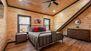 A wooden-paneled bedroom with a bed, nightstands, a dresser, and a ceiling fan. - NEW, INDOOR POOL, GAME ROOM, BUNK ROOM, HOT TUB (Sevierville)