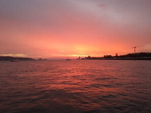 Ein Sonnenuntergang über ruhigem Wasser mit Booten und einer fernen Skyline.