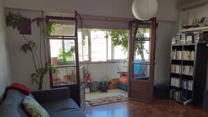 Una sala de estar con un sofá, una estantería y vistas al exterior a través de un ventanal.