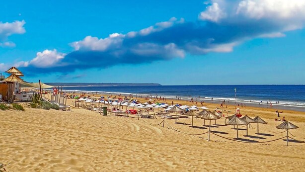 Una playa con sombrillas y sillas, una torre de salvavidas y el océano al fondo.