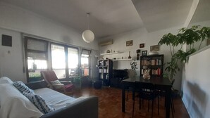 Una sala de estar con un sofá, una mesa de comedor con sillas, una estantería y una planta en maceta.