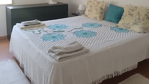 A bedroom with a bed, a bedside table, a lamp, and a window with blinds. - Delta Marina Vilamoura Center Flat (Loulé)