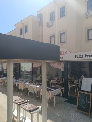 Un café al aire libre con mesas y sillas, un letrero que dice 'MAR' y 'Peixe Fres', y una pizarra con el menú.