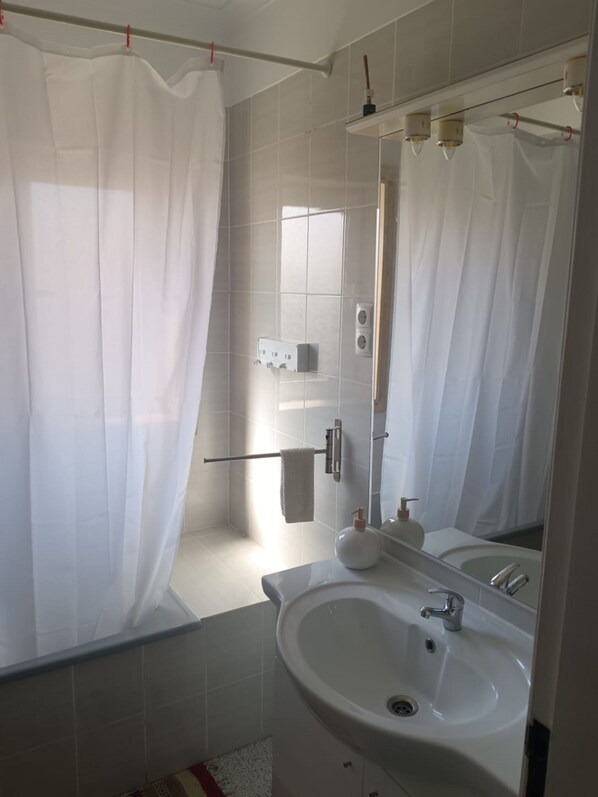 Een badkamer met een wit wastafelmeubel, spiegel en douchegordijn.