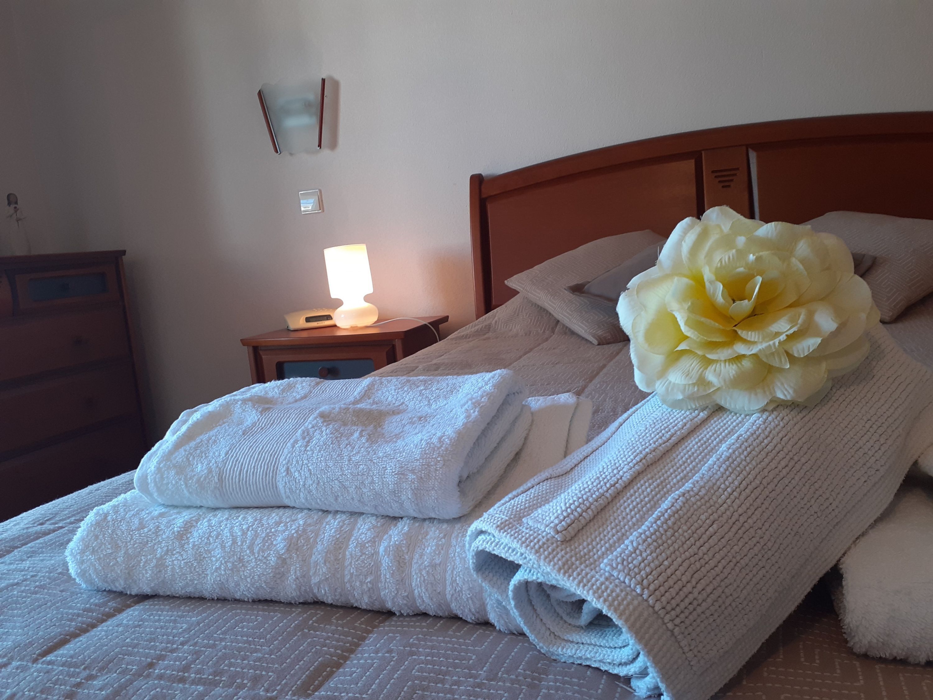 Una cama bien hecha con toallas dobladas y una flor grande sobre la almohada.