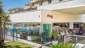 A modern building with a 'Plaza Bar' sign, glass walls, outdoor seating, and a pool area. - Vplaza Private Garage Balcony Pool View Flat (Portimão)