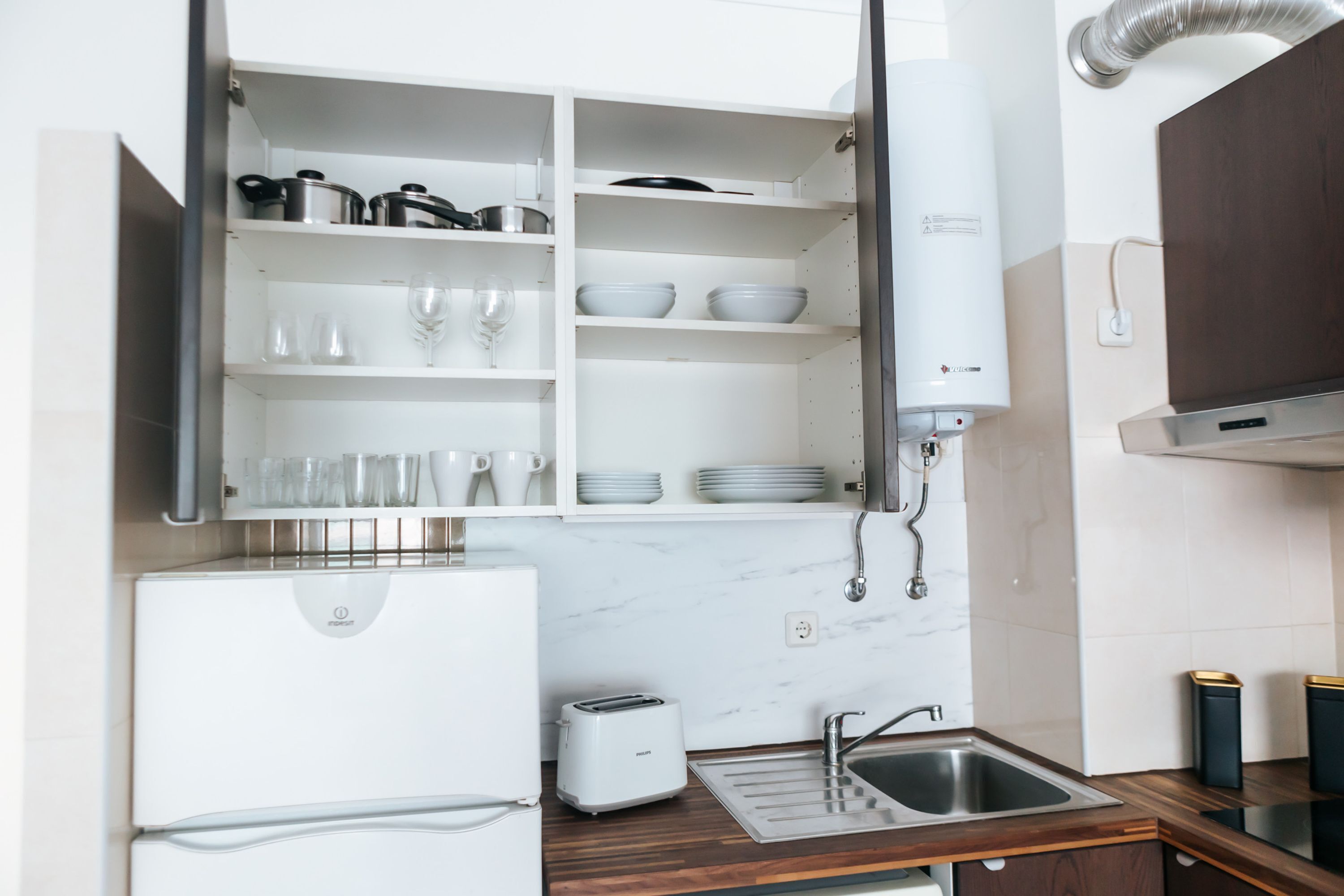 A modern kitchen with white cabinetry, a built-in oven, a toaster, and a stainless steel sink.