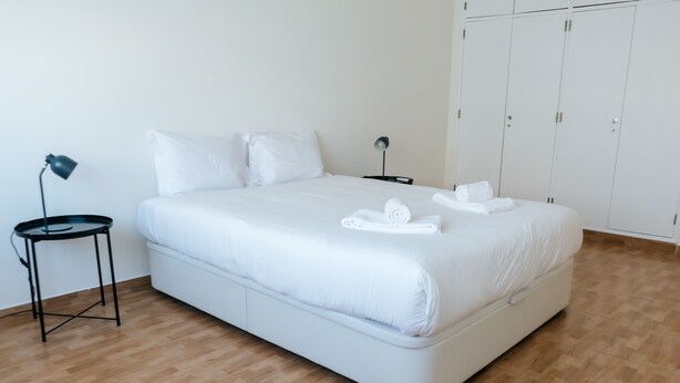 A neatly made bed with white linens and towels, a small table with a lamp, and a wardrobe with multiple doors. - Lisboa Almirante Reis Downtown Flat E (Lisbon)